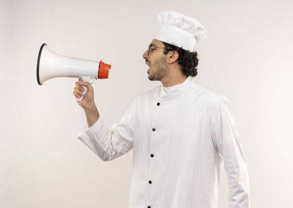 男性站在侧视图中 年轻的男厨师穿着厨师制服 戴着眼镜 隔着白墙上的扬声器讲话穿着个人资料站立