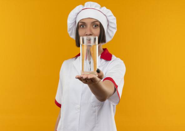 空间令人印象深刻的年轻女厨师在厨师制服伸出一杯水对相机孤立的橙色与复制空间走向橙色制服