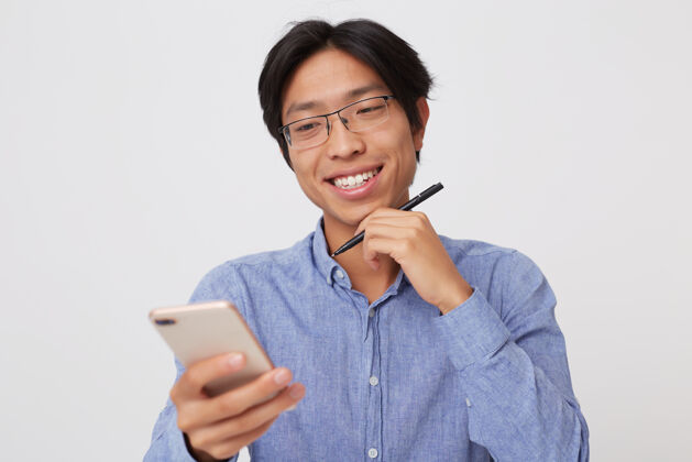 年轻人斯米利格的肖像成功的亚洲年轻商人戴眼镜和蓝色衬衫使用手机隔离在白色的墙壁自信电话学生