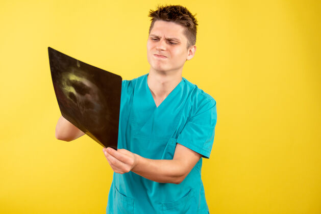 医院正面图身穿医疗服的年轻男医生拿着黄色背景的x光片持有健康成人