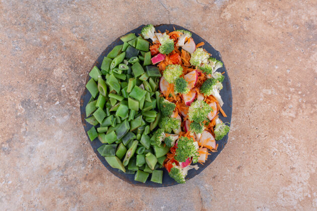 托盘一小盘混合蔬菜沙拉和切碎的豆荚放在大理石表面萝卜胡萝卜脉冲
