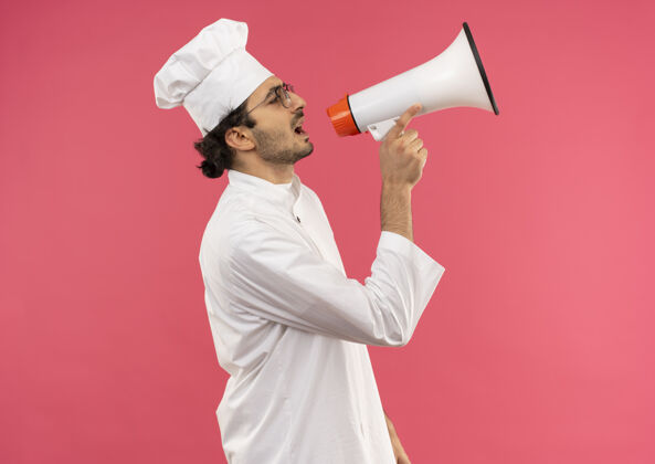 站立站在侧视图中 年轻的男厨师穿着厨师制服 戴着眼镜 隔着粉色墙上的扬声器讲话制服烹饪眼镜