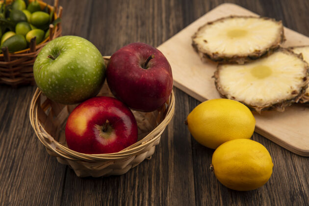 纸板新鲜的五颜六色的苹果放在木桶上 菠萝放在木制的厨房板上 金盏花放在木桶上 柠檬被隔离在木墙上顶部农业新鲜