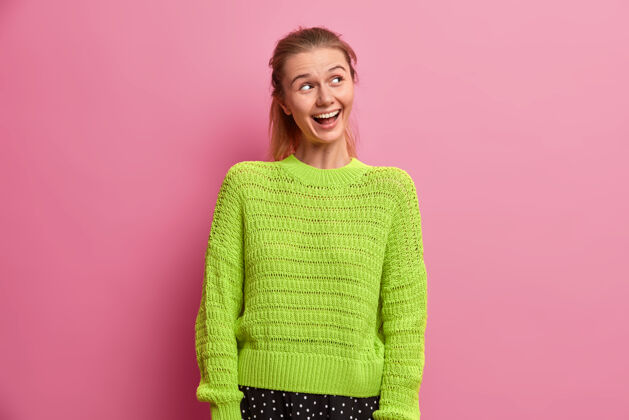 年轻快乐快乐的欧洲千禧一代女孩 穿着绿色针织毛衣 带着牙齿般的微笑 专注在一旁 享受生活 对积极的事情咯咯地笑 注意到正确的事情搞笑成人外观时尚