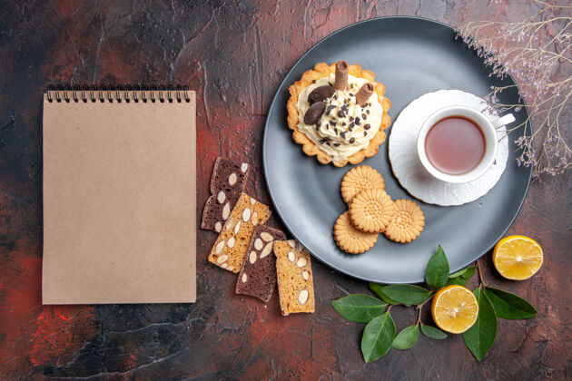 俯瞰美味的奶油蛋糕 茶和饼干放在深色的桌子上甜甜的蛋糕甜点蛋糕顶笔记本