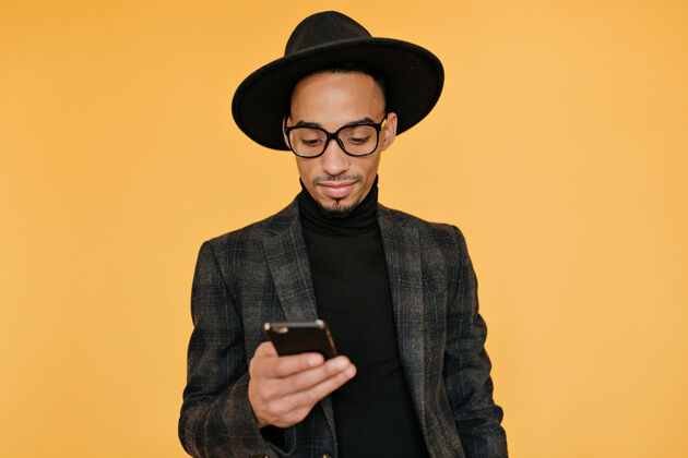 男人室内照片中 身着华丽服装的黑人年轻人手持智能手机情绪激动的非洲小伙子微笑着等待电话通话优雅手机