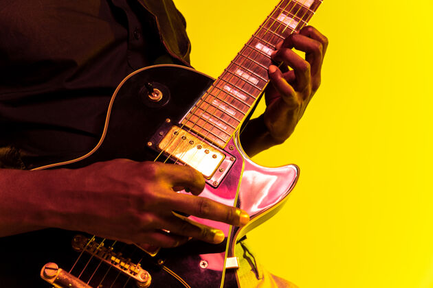 成人年轻的非洲裔美国音乐家在霓虹灯下像摇滚明星一样在黄色背景下弹吉他娱乐天才音乐会