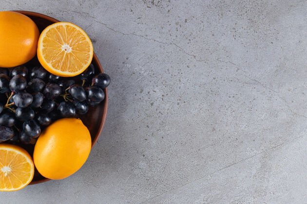 有机石头桌上放着一大盘新鲜的黑葡萄和橙子葡萄多汁美味
