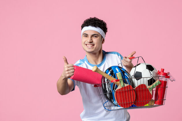 健身房正面图快乐的年轻男子穿着运动服 篮子里装满了运动用品体育球员粉红色