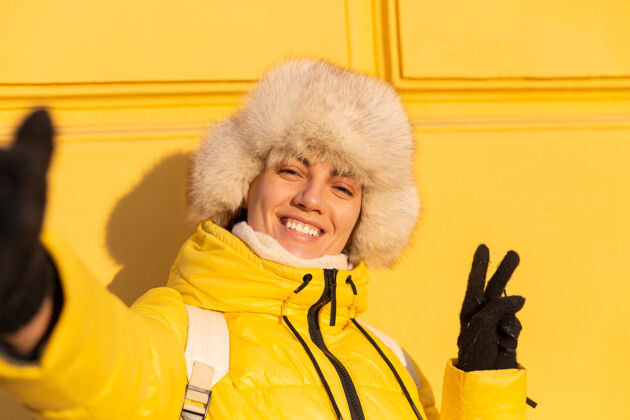 漂亮在阳光明媚的日子里 一个戴着温暖的俄罗斯西伯利亚帽子的快乐女人的肖像画 她在冬天穿着雪白的zabas 对着黄色的墙壁微笑着寒冷街头温暖