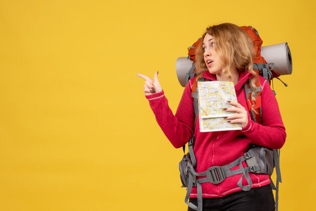 地图俯视图：戴着医用面罩的年轻出其不意的旅行女孩正在收拾行李 手里拿着指向后面的地图成人抱肖像