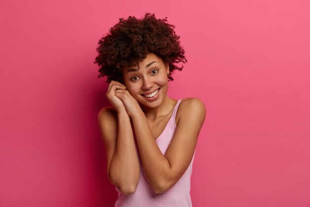 脸独立拍摄的美丽健康的女人微笑温柔 歪着头 享受愉快的谈话 穿着随意 快乐 模型对粉红色的墙壁积极的情绪概念人类黑发女士