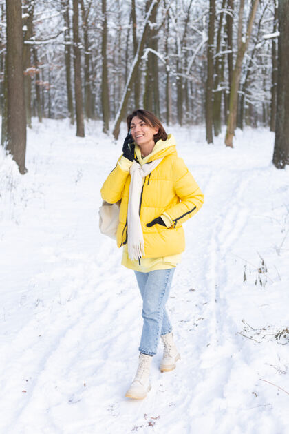 年轻心情愉快的快乐女人漫步在雪域的冬日森林里 愉快地聊着电话 享受着公园里的户外时光节日帽子女性