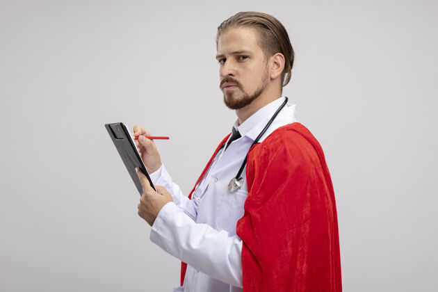 年轻自信的年轻超级英雄穿着医用长袍 听诊器写在剪贴板上 隔离在白色背景上家伙医疗听诊器