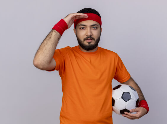 球戴着头带和腕带的年轻运动型男子看着相机 手拿球孤立在白色背景上手相机头带