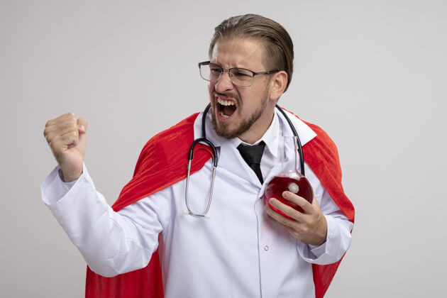 玻璃兴奋的年轻超级英雄穿着医用长袍 戴着听诊器和眼镜 手里拿着装满红色液体的化学玻璃瓶 在白色背景上显示“是”的手势眼镜年轻医疗