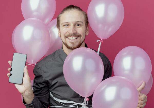帅哥笑容可掬的帅哥拿着氦气球站着 手机被隔离气球粉色氦