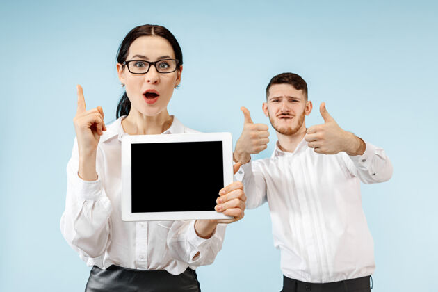 关系在蓝色工作室背景上 惊讶的商务男女微笑着 展示着笔记本电脑或平板电脑的空屏幕兴奋夫妻女性