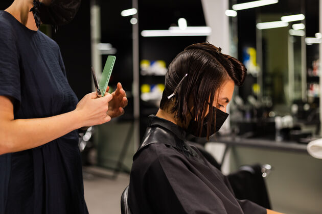 发廊一个专业的女理发师给客户理发这个女孩戴着面具坐在美容院里发廊发型师设备