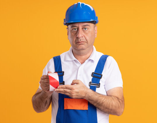 人自信的白人成年建筑工人穿着制服拿着橙色的透明胶带成年人建筑工人胶带