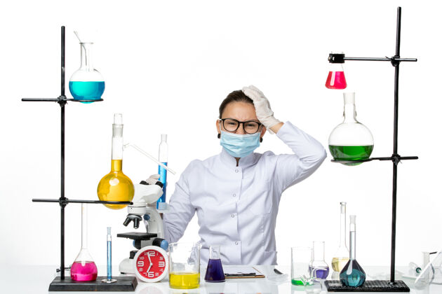 病毒前视图：穿着医疗服的女化学家 戴着面罩 拿着一个装有蓝色溶液的烧瓶 背景是白色的病毒化学实验室的covidsplash医生医学实验室