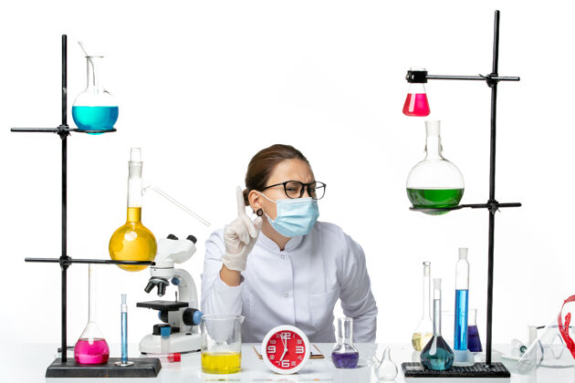 溶液前视图：穿着医疗服的女化学家戴着面罩坐在白色背景上摆出解决方案化学实验室病毒冠状病毒-飞溅套装病毒面罩