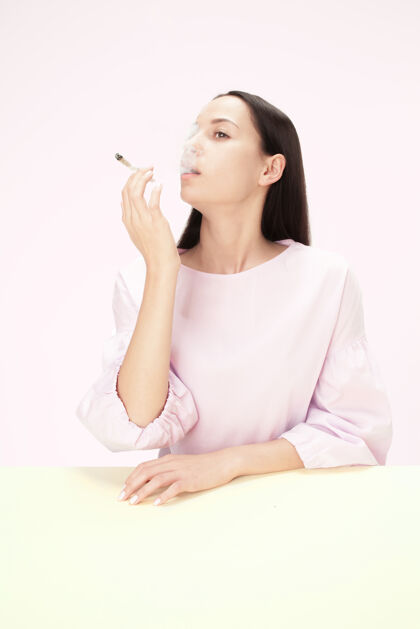 悲伤坐在画室桌子旁抽烟的年轻女子流行的颜色极简风格的白种女孩肖像 带复印空间孤独香烟烟草
