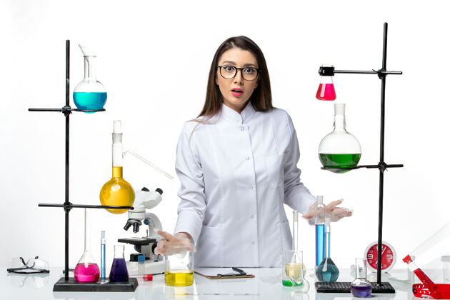 药品正面图：穿着无菌医疗服的女化学家站在桌子旁 拿着白色背景病毒疾病的解决方案-流行科学医生医疗人