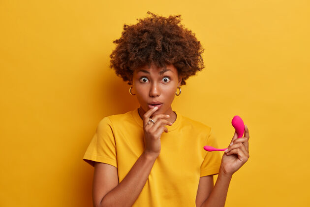室内惊讶的黑皮肤女人震惊的创新技术在性领域 持有粉红色的橡胶智能振动器 可以与您现有的技术同步 通过蓝牙连接到手机非洲惊喜情色