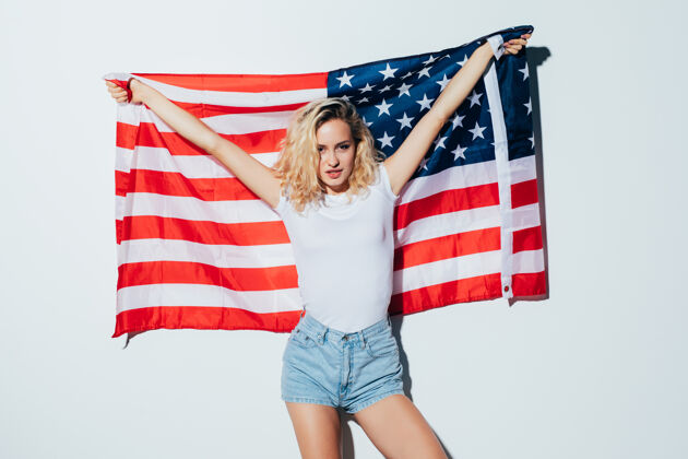 内容美国金发女子举着美国国旗隔着一堵白墙学习脸微笑