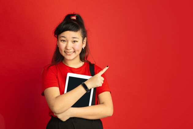亚洲人在红色工作室背景上孤立的亚洲青少年肖像休闲风格的美丽的深褐色女性模特人类情感的概念 面部表情 销售 广告用平板电脑指着 微笑公司人年轻人