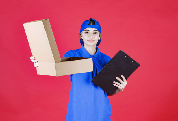 送货穿着蓝色制服的女快递员拿着一个黑色的文件夹 把纸板外卖箱递给顾客成人智能休闲