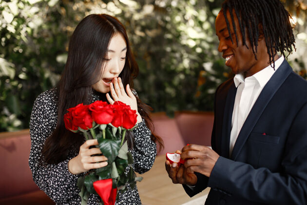 兴奋一个黑人在咖啡馆向一个中国女孩献上了手和心两个花束周年纪念