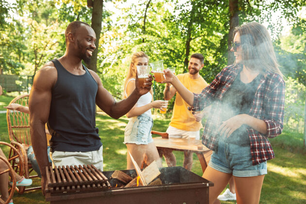 公园一群快乐的朋友在阳光明媚的日子里举行啤酒和烧烤派对一起在户外的森林空地或后院休息欢庆和放松 欢笑夏日生活方式 友谊理念烧烤午餐烧烤