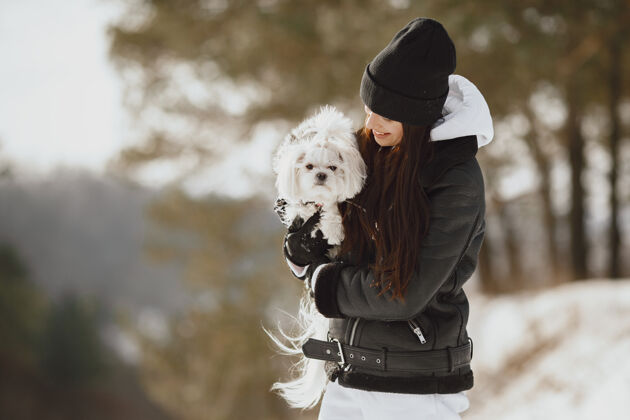 年轻在冬季公园散步的可爱女孩穿着棕色夹克的女人牵着狗的女人友谊小狗寒冷