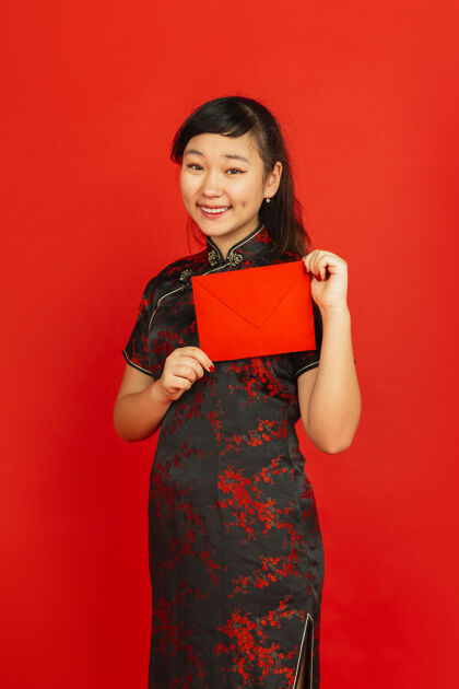 愿望2020中国新年红色背景上孤立的亚洲少女肖像身着传统服装的女模特看起来很开心 微笑着拿着红包庆祝 节日 情感传统服装照明