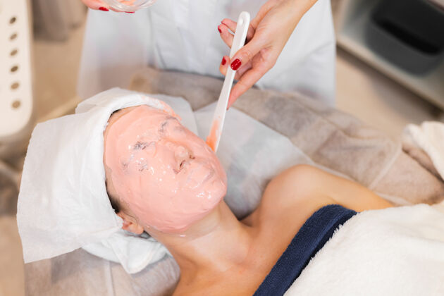 服务美容师用抹刀在女人脸上敷海藻酸钠面膜皮肤沙龙面部