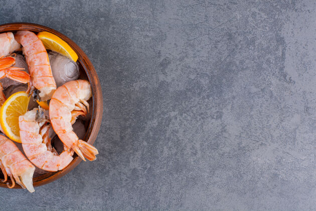 小吃一个木制盘子 上面放着美味的虾仁 冰块和柠檬片 背景是石头虾烹饪晚餐