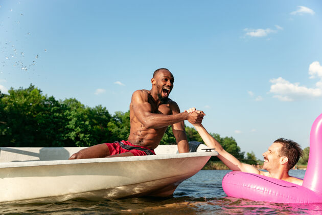 家庭一群快乐的朋友在河中嬉笑 泼水 游泳阳光明媚的日子里 穿着泳装的快乐男人在河边划船夏日 友谊 度假 周末的概念一起友谊时刻