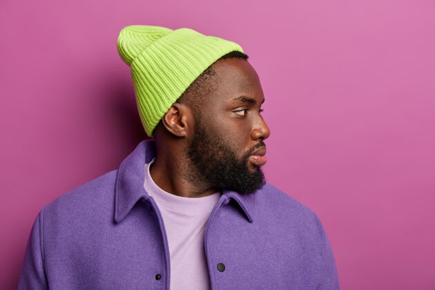 阳刚照片中的黑人潮人表情凝神地站在一边 戴着绿色的帽子 紫色的夹克 想着什么姿势男人旁白