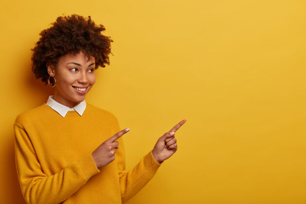 靠边漂亮的卷发女人的室内镜头指向右上角 在空白处展示漂亮的广告 穿着整洁的黄色套头衫非洲裔指标建议