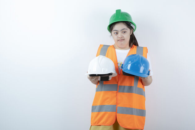 表情戴着安全帽的年轻女建筑工人戴着头盔翻过白墙头盔唐氏综合症背心
