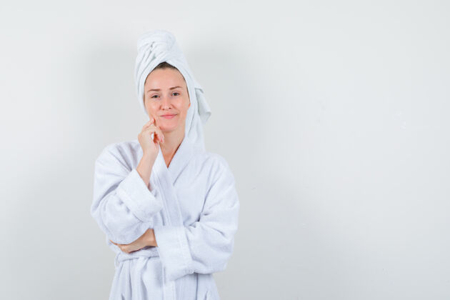 微笑年轻女子站在思考的姿势在白色浴袍 毛巾 并期待乐观前视图黑发成人魅力
