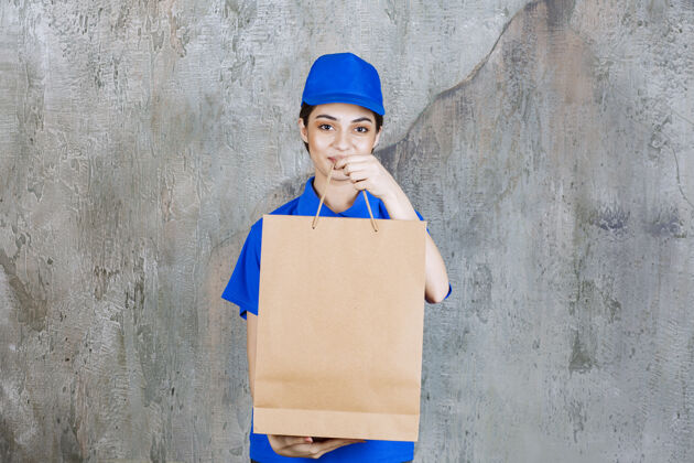 姿势穿着蓝色制服的女服务人员拿着一个硬纸板购物袋递给顾客制服年轻人员工