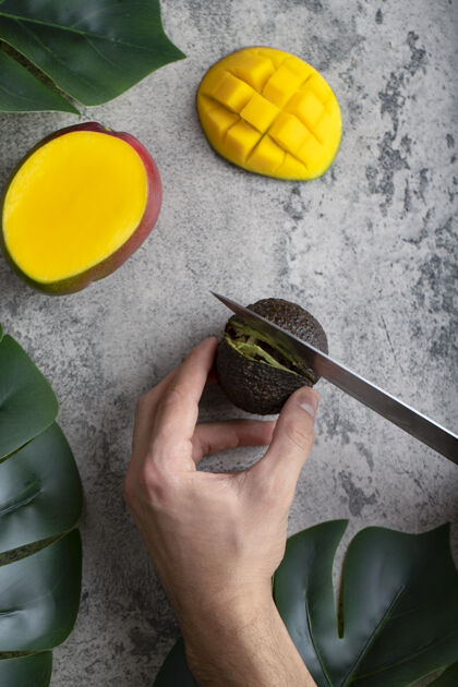 一半男手用刀在石桌上切新鲜成熟的鳄梨热带块刀