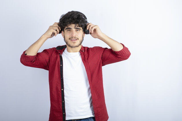 黑发戴着耳机的年轻人站在白色背景上的照片高质量的照片音乐年轻男性