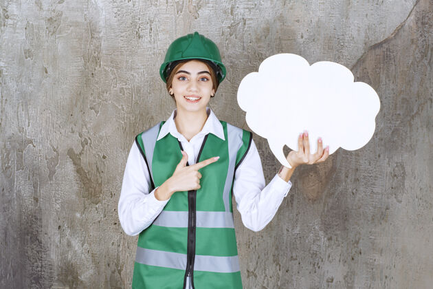 姿势身穿绿色制服 头戴头盔 手持云彩形状信息板的女工程师规则年轻人标准