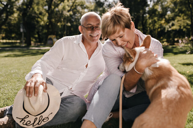 两个迷人的女人 短发微笑 玩高尔基犬 坐在草地上 白发苍苍的男人 戴着帽子 穿着白衬衫肖像女士退休