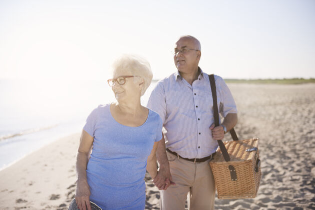 假日寻找一个完美的地方野餐老年夫妇在海滩 退休和暑假的概念日落牵手散步