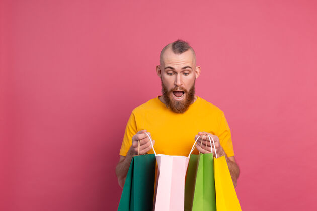 商场快乐的胡须积极的男人休闲装扮与五颜六色的购物袋工作室粉红色的背景惊喜昂贵消费